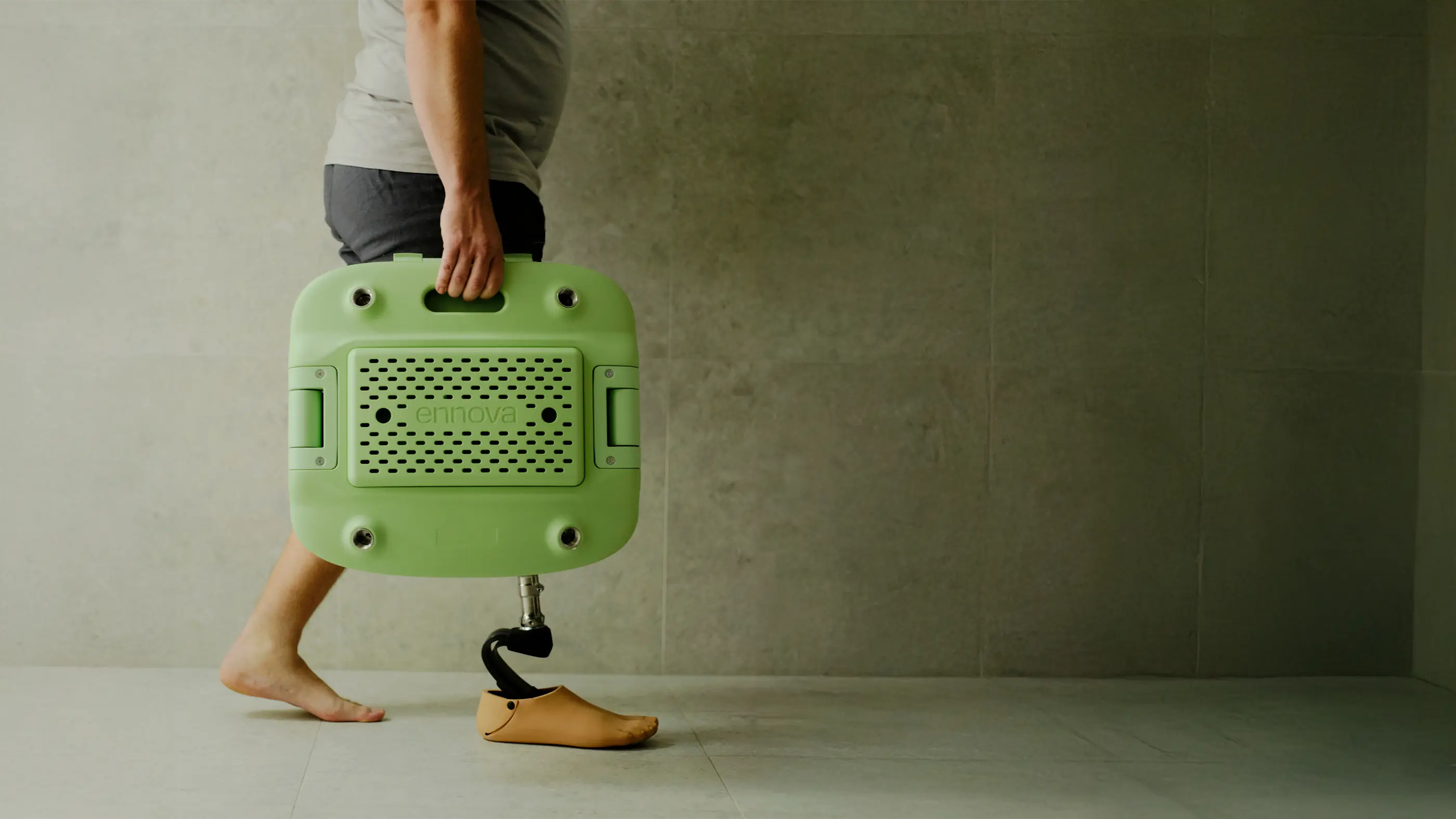 A person with a prosthetic leg is carrying a packed down, transportable pastel green Oasis shower chair with one hand.