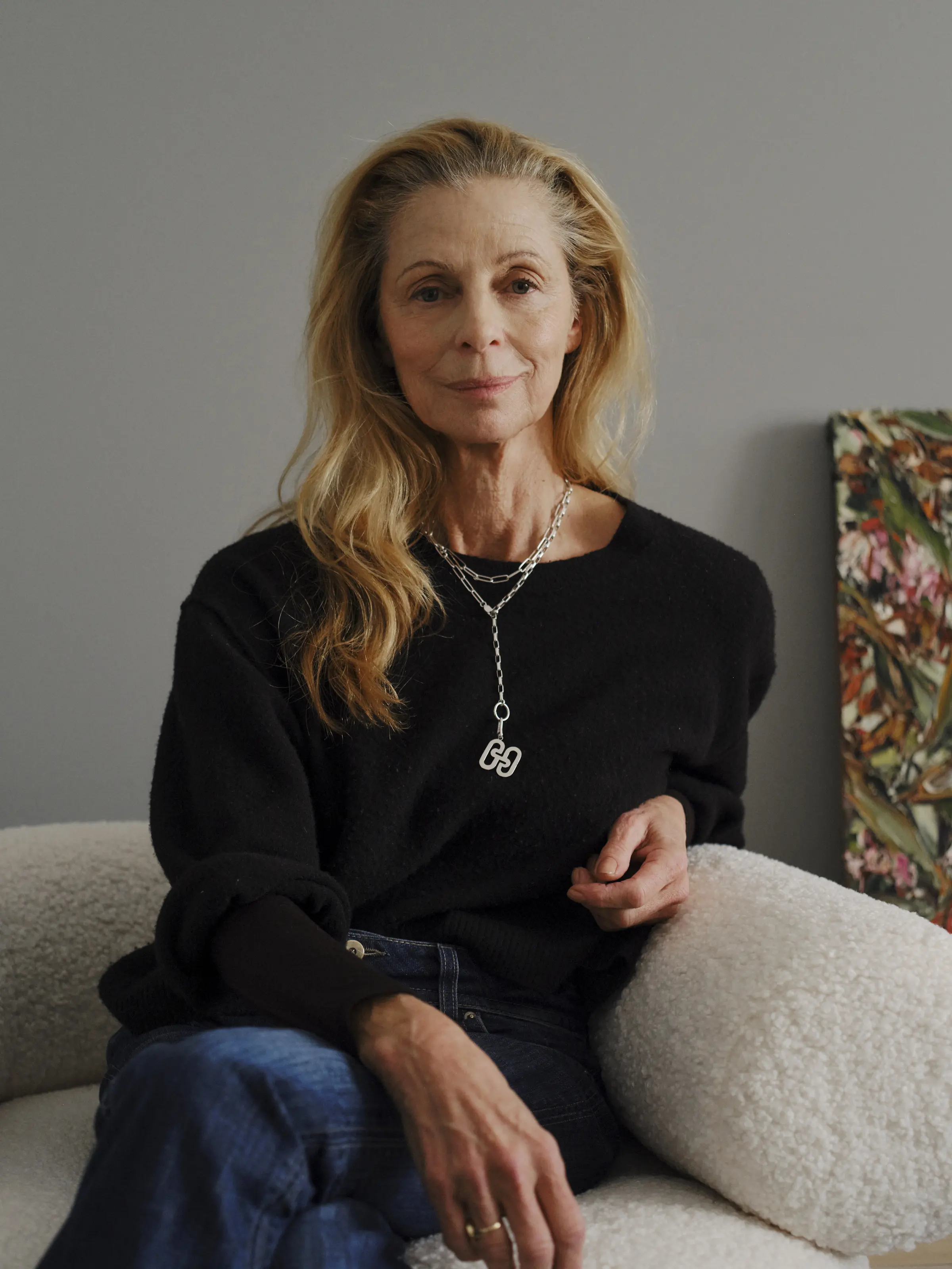 A picture of an older lady with long blond hair wearing a black top and denim jeans with silver jewellery.