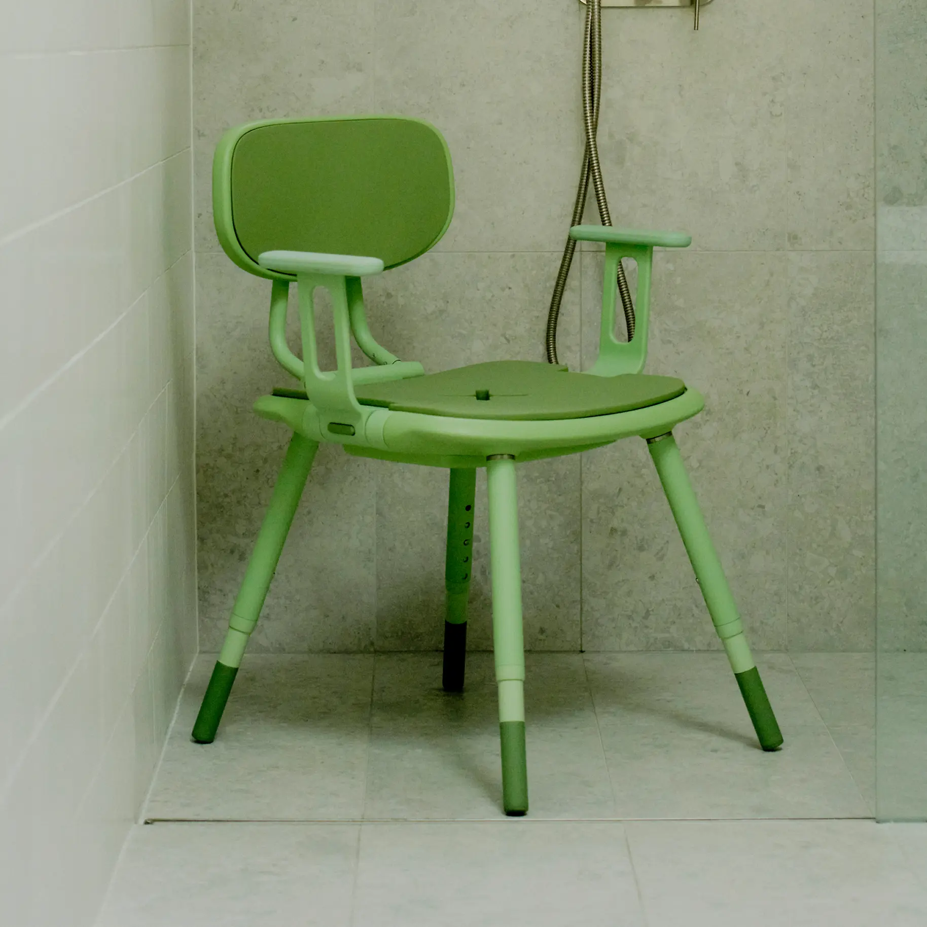 A pastel green Oasis shower chair is positioned in a tiled shower. The foldable armrests are up and ready.
