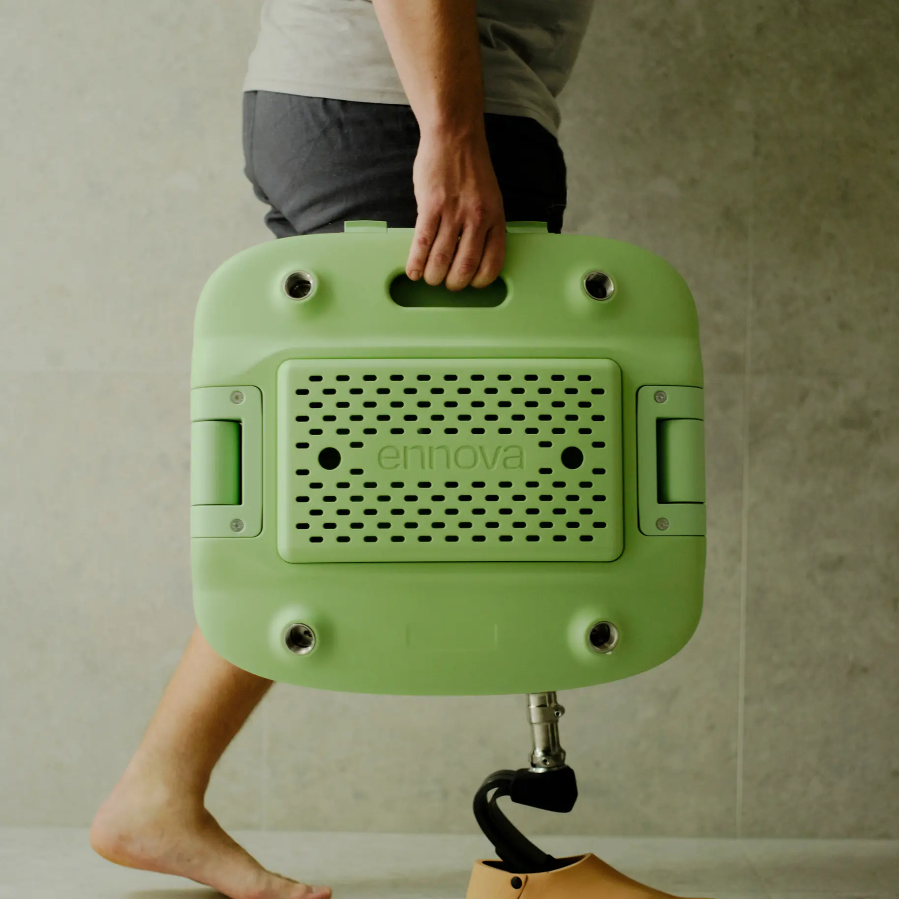 A person with a prosthetic leg is carrying a packed down, transportable Oasis shower chair with one hand.