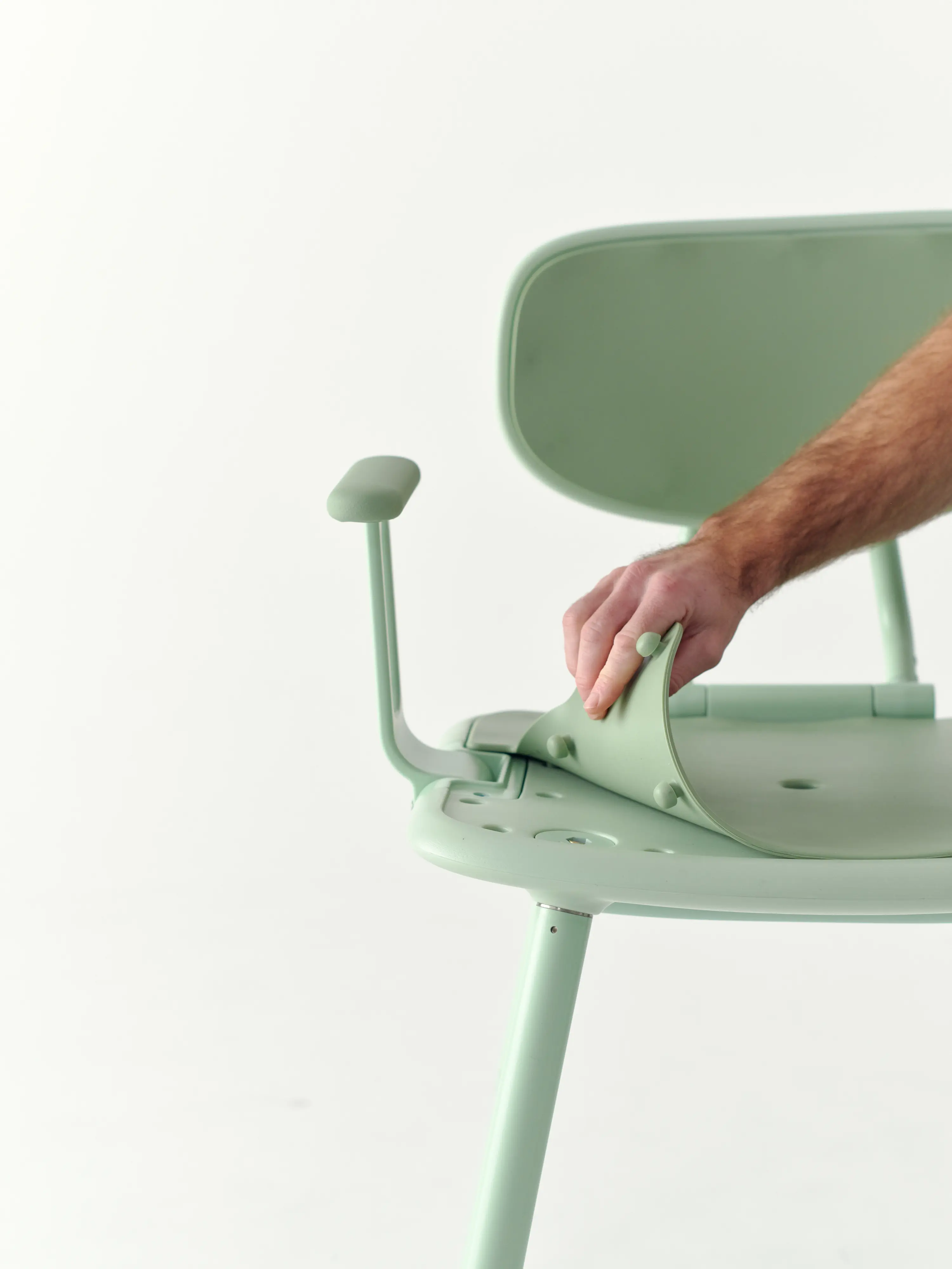 A hand pulls the silicone seat pad off the Green Oasis Shower Chair