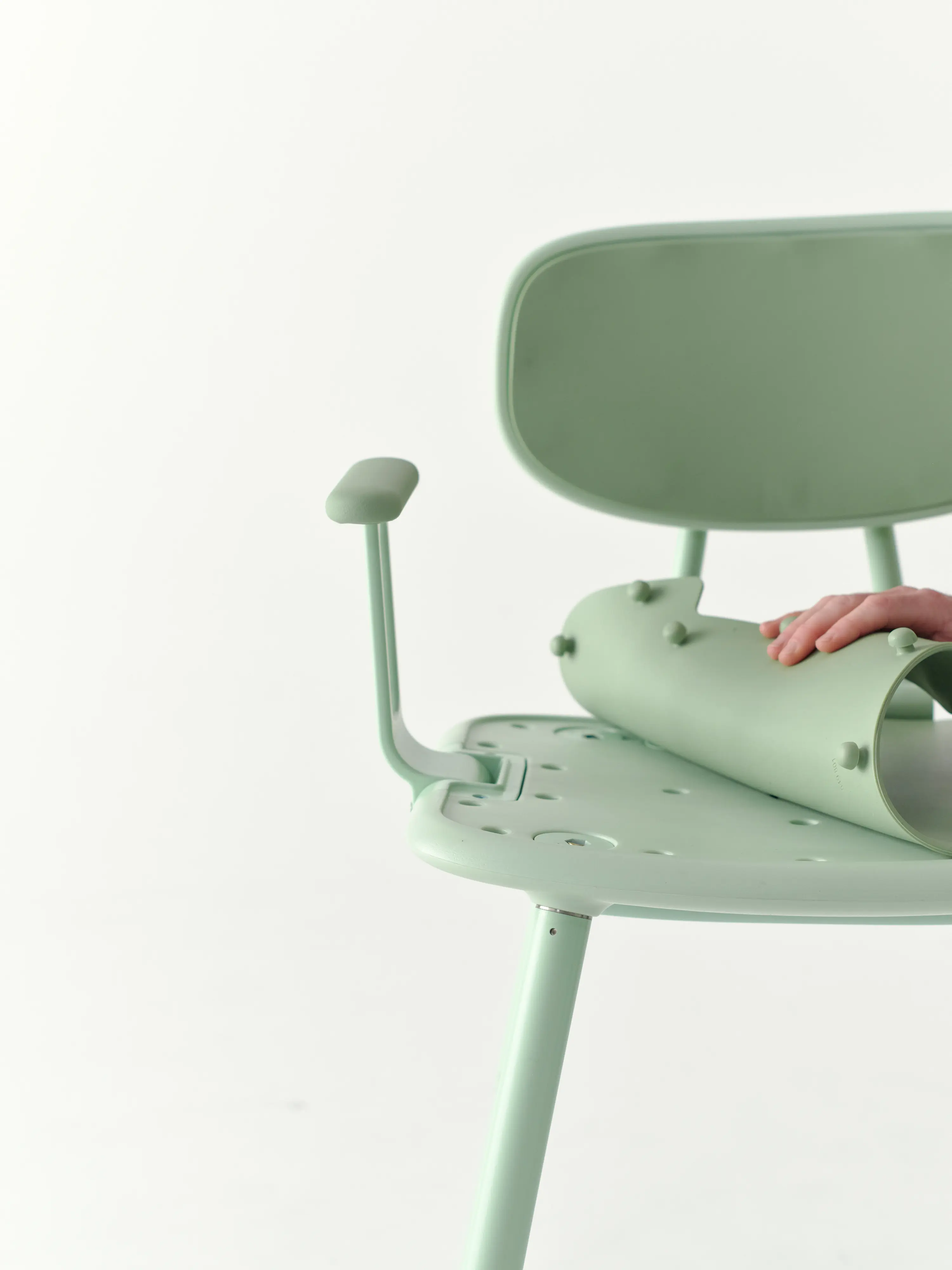 A hand pulls the silicone seat pad off the Green Oasis Shower Chair